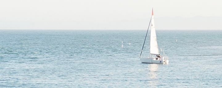 Sailboat with white sails on calm blue ocean water under clear sky